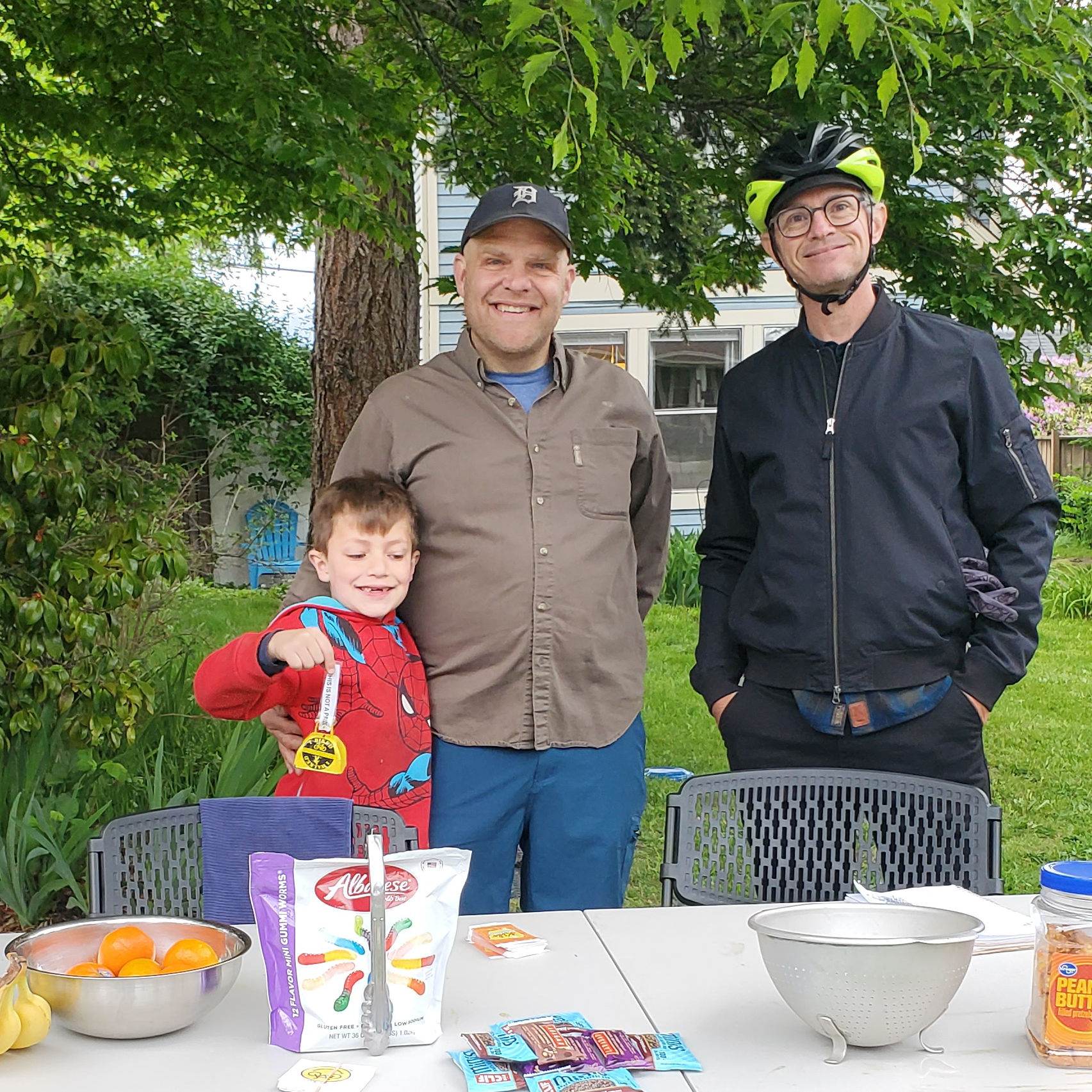 Two adults and one child standing behind a table with snacks.