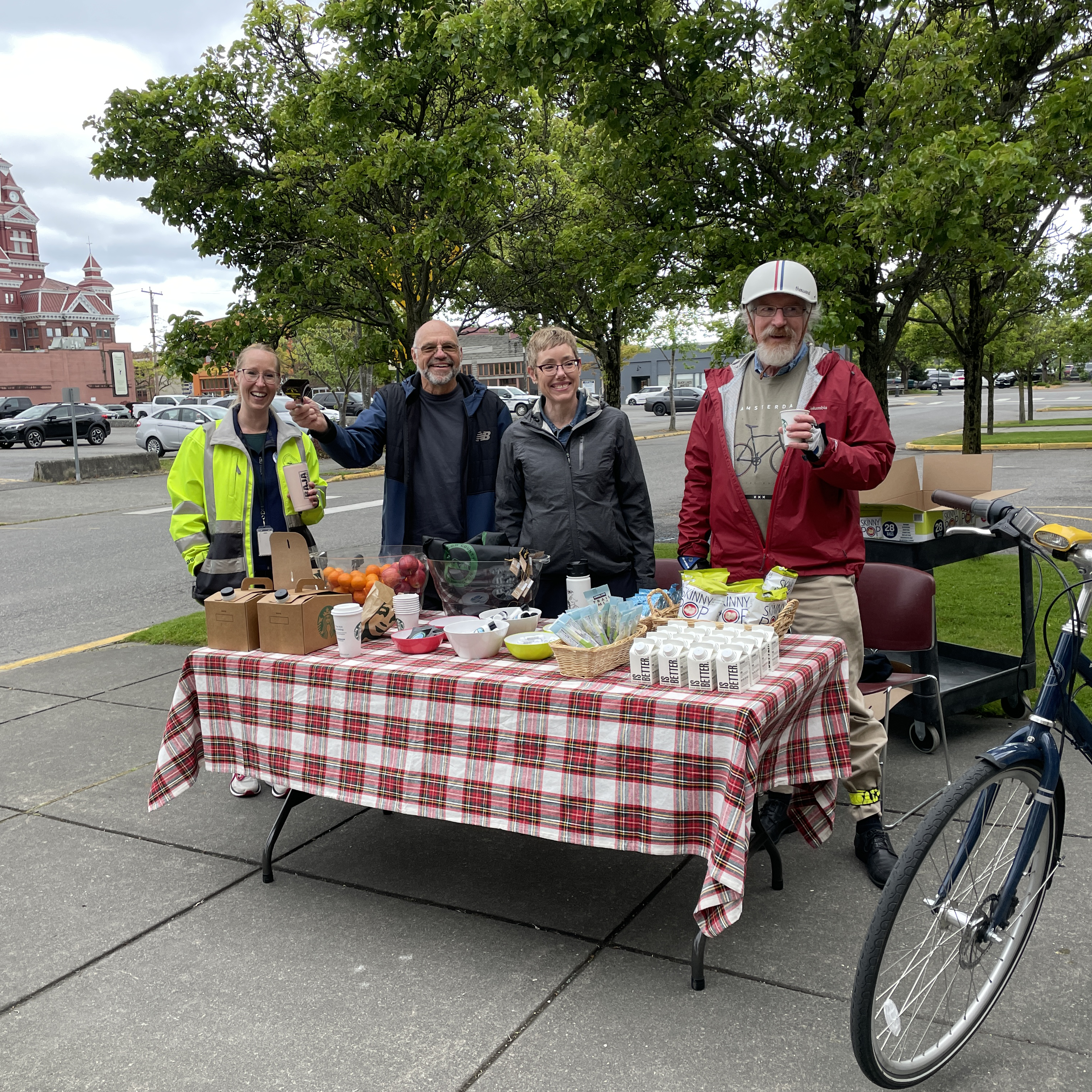 Four people including a cyclist with helmet standing behind a table with snacks.
